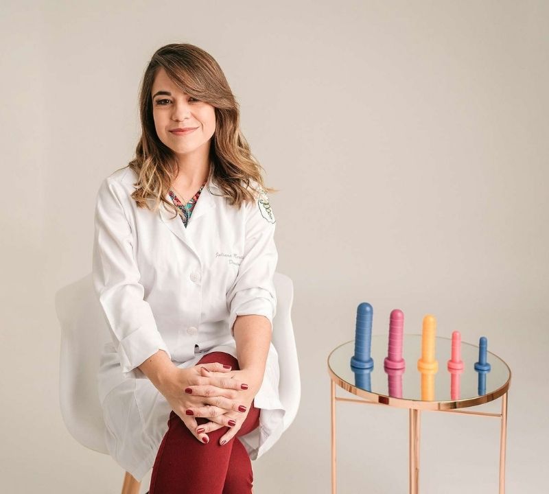 Juliana Donatoni, fisioterapeuta pélvica, sentada à mesa com instrumentos de fisioterapia pélvica em consultório em Salto/SP